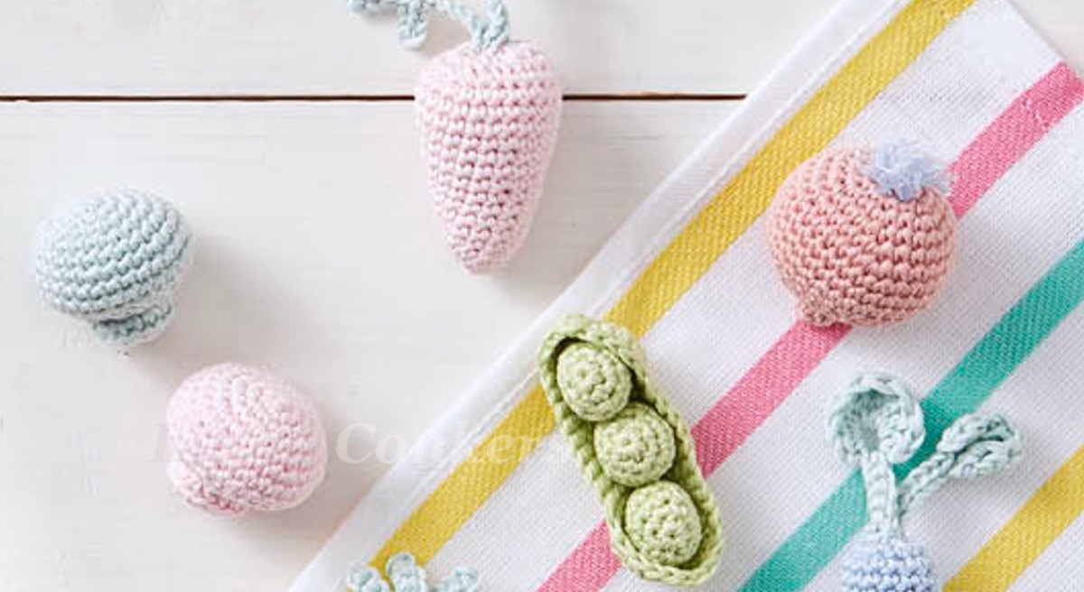 mini crocheted vegetables in pastel colours including carrots, mushrooms, a pod of peas and radishes.