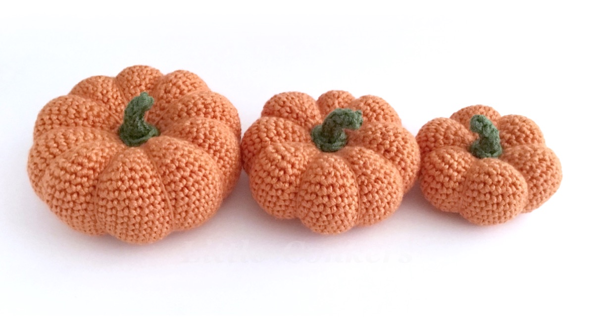 Crochet mini pumpkin ornaments in three sizes, made in orange yarn with green yarn stalks.