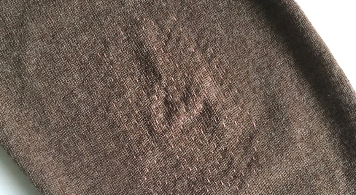 A fine knit brown jumpere reinforced on the elbows with a regular pattern of pink stitches.